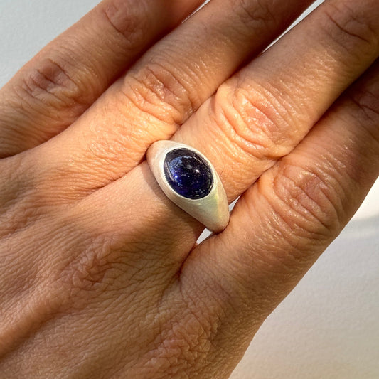 Hand wearing a silver ring with a blue gemstone on a white background