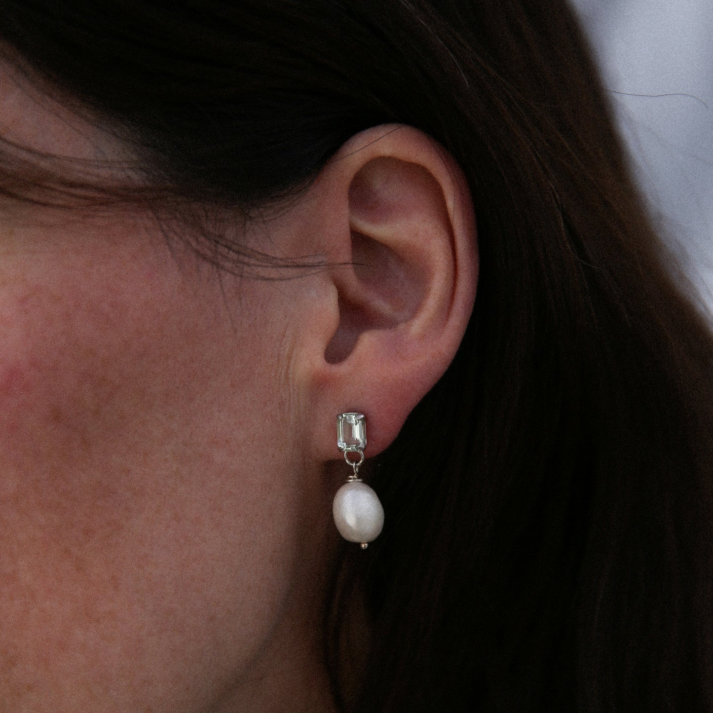 Close-up of an ear wearing a pearl earring with a clear gemstone.
