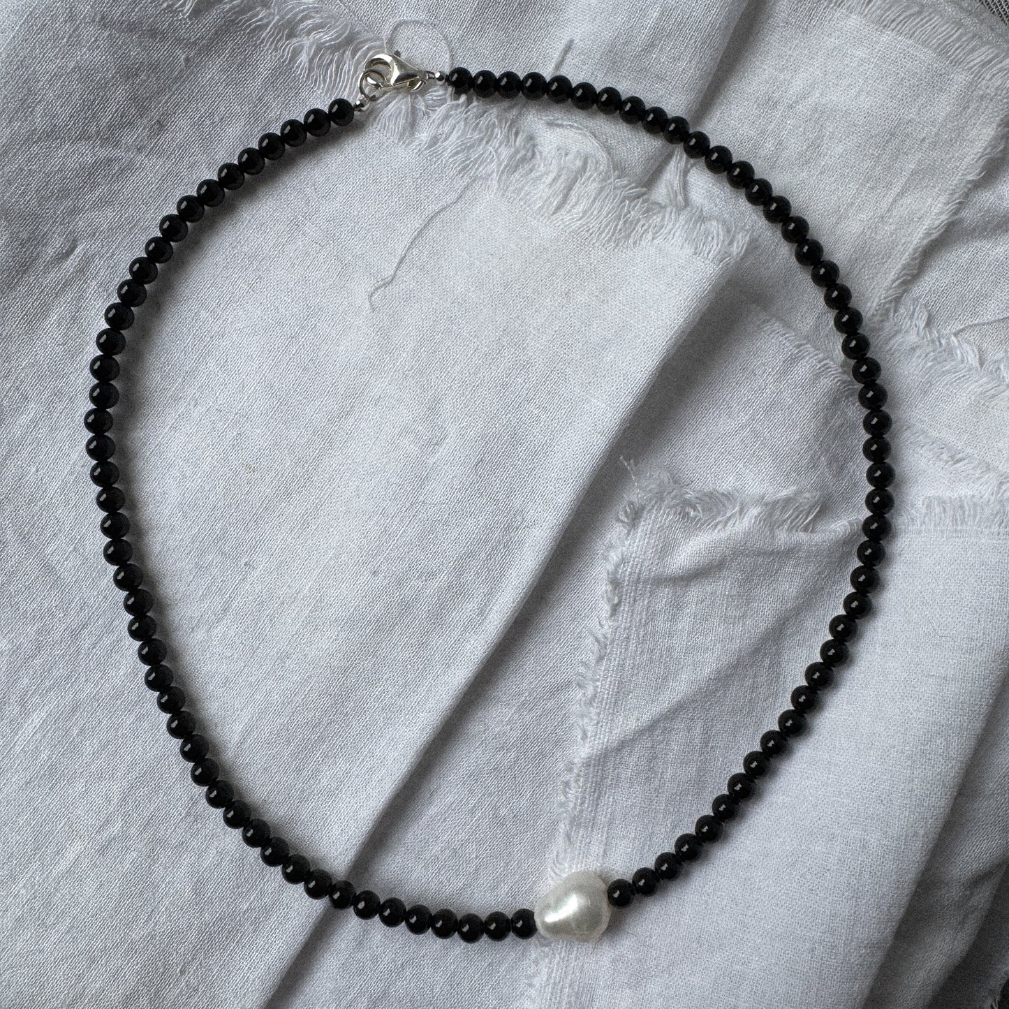 Necklace with black beads and a pearl on a light gray fabric background