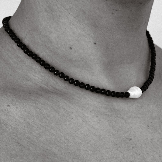 Black beaded necklace with a white accent on a person's neck against a neutral background