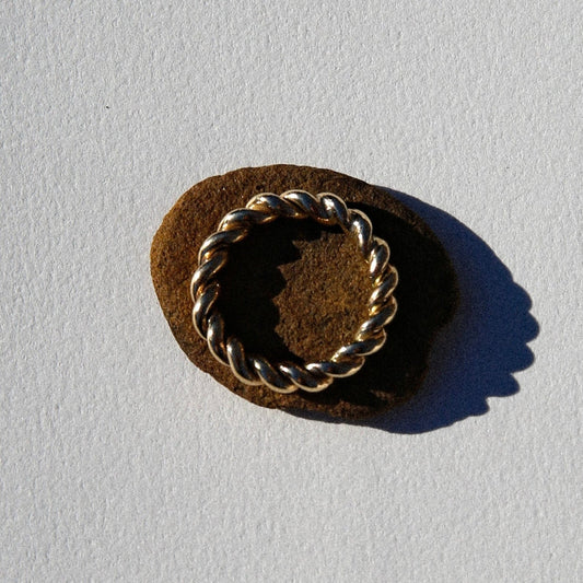 Gold ring with rope design on a brown stone against a light gray background