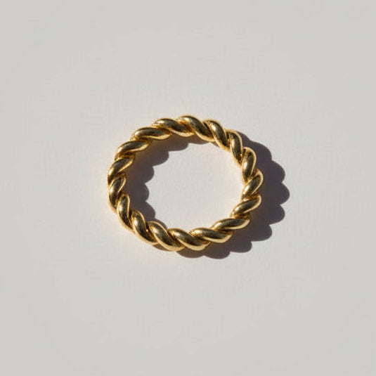 Gold ring with rope design on a brown stone against a light gray background