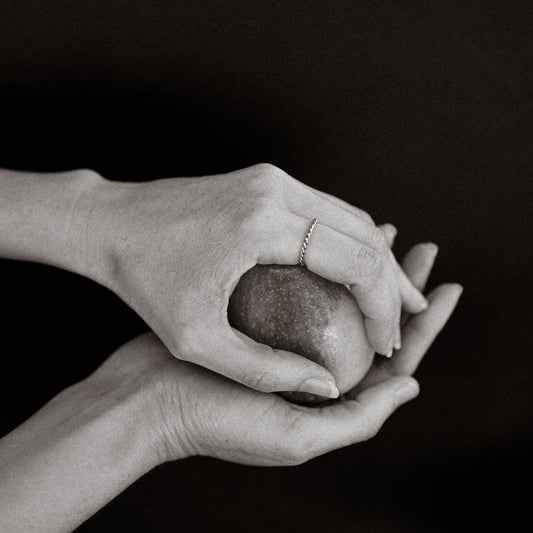 Black and white photo of hands holding a heart-shaped object against a dark background