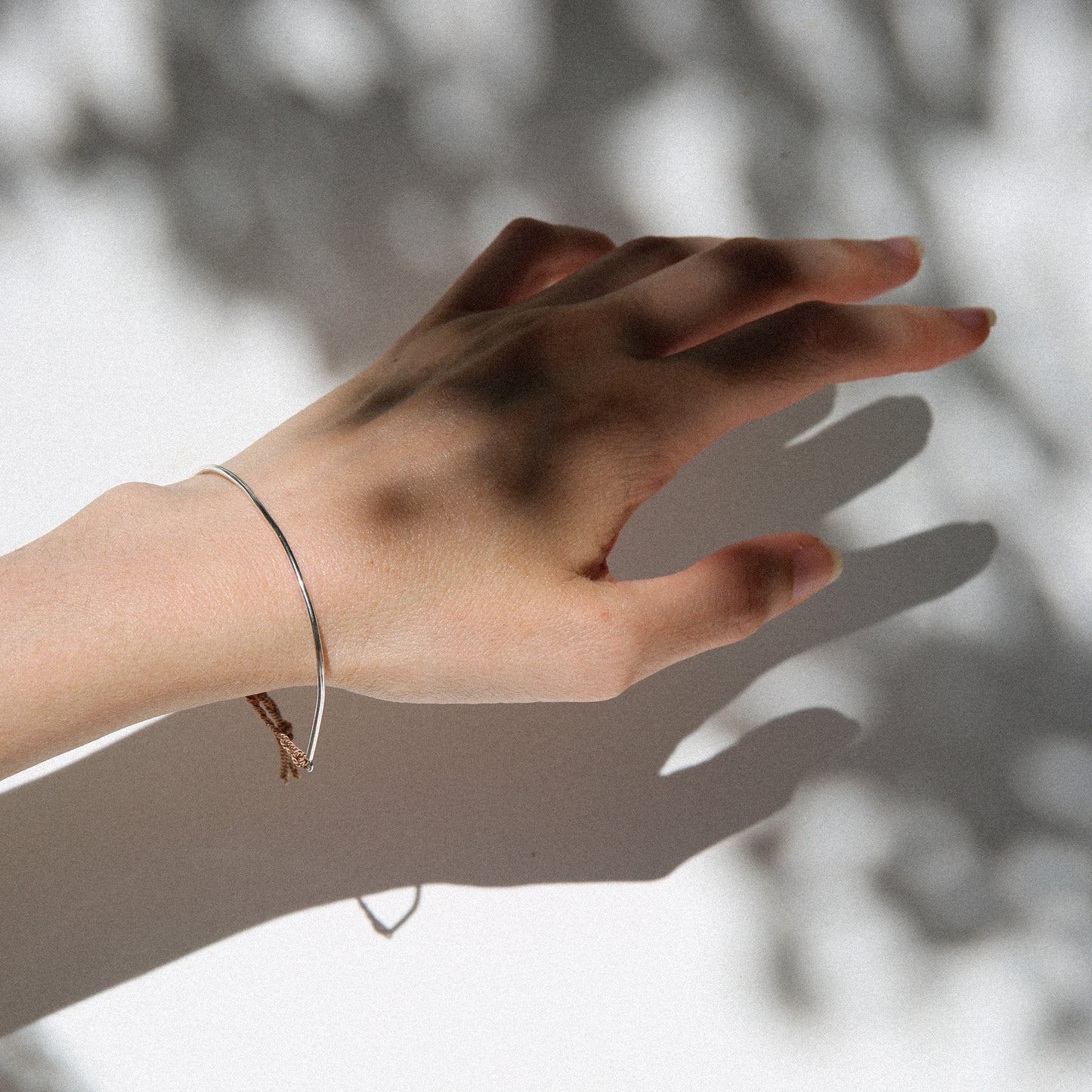 Hand with a bracelet casting a shadow on a light background