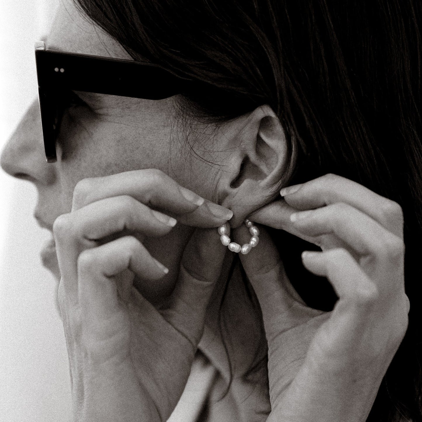 Person wearing sunglasses and adjusting an earring with a plain background