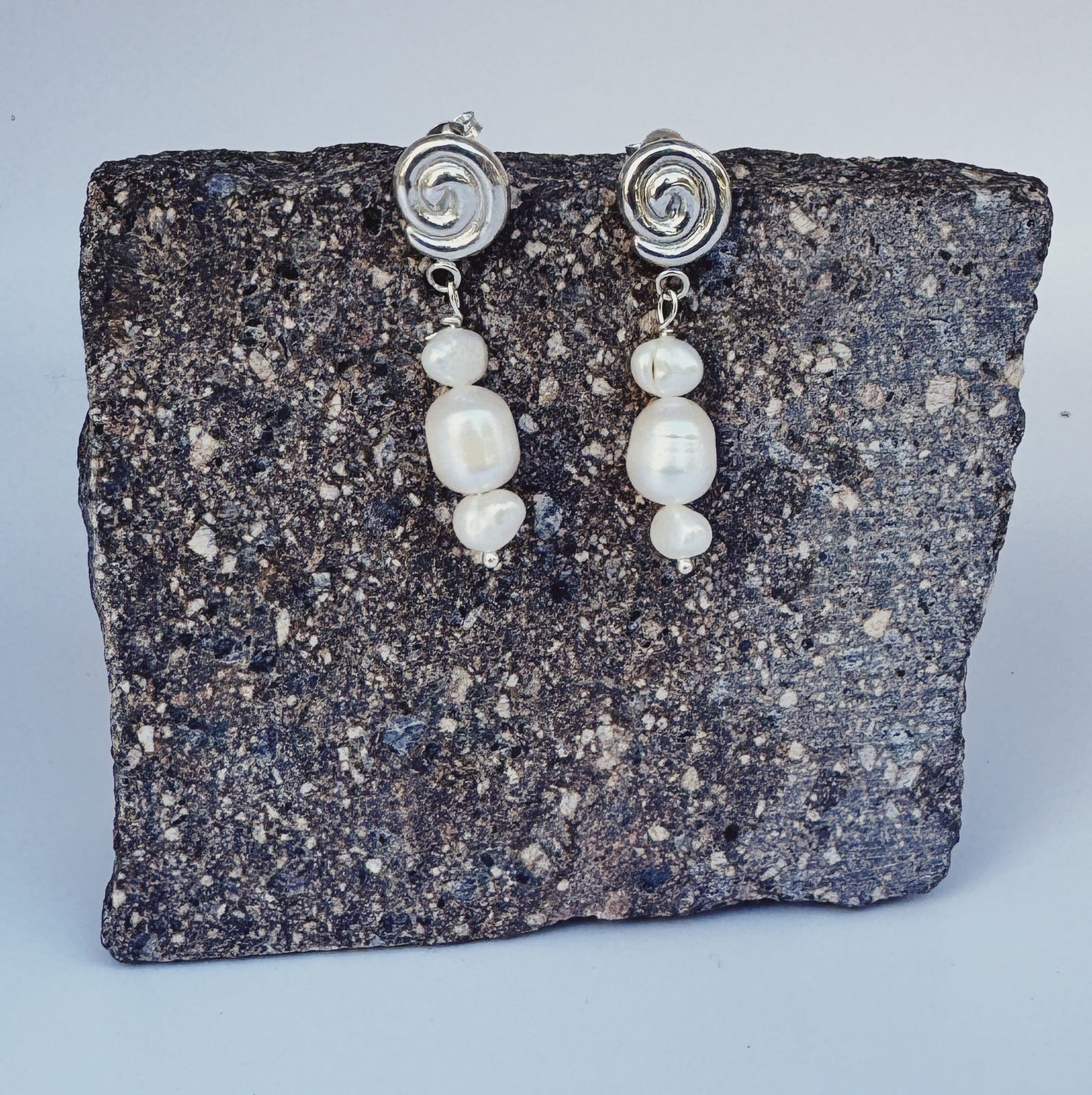 Pair of pearl earrings with silver spiral tops on a stone surface