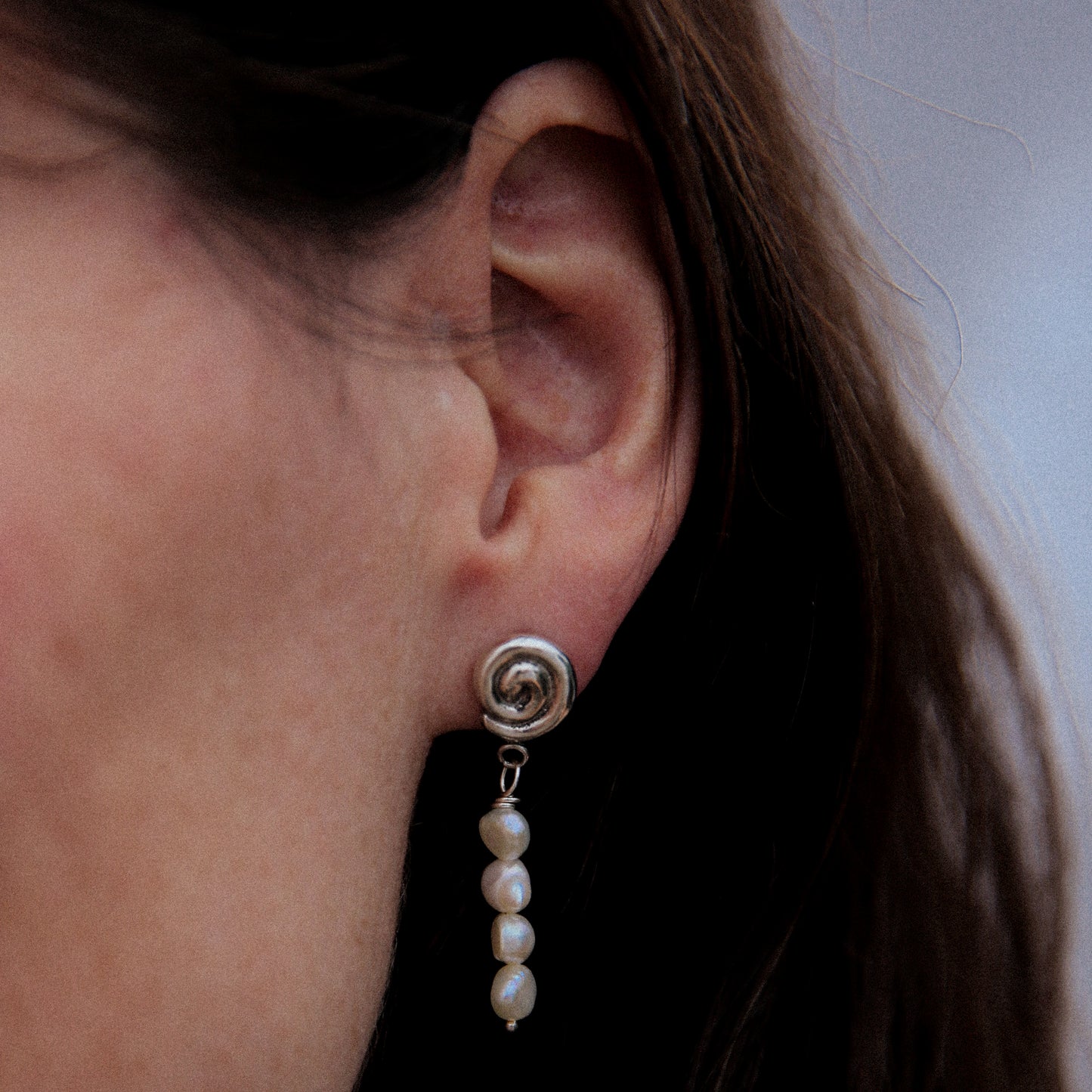 Close-up of an ear wearing a silver earring with pearl drop
