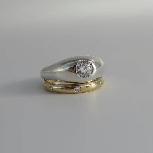 A two-tone wedding ring set featuring a silver band with a round clear gemstone and a yellow gold band with small inset diamonds, displayed on a neutral gray background.