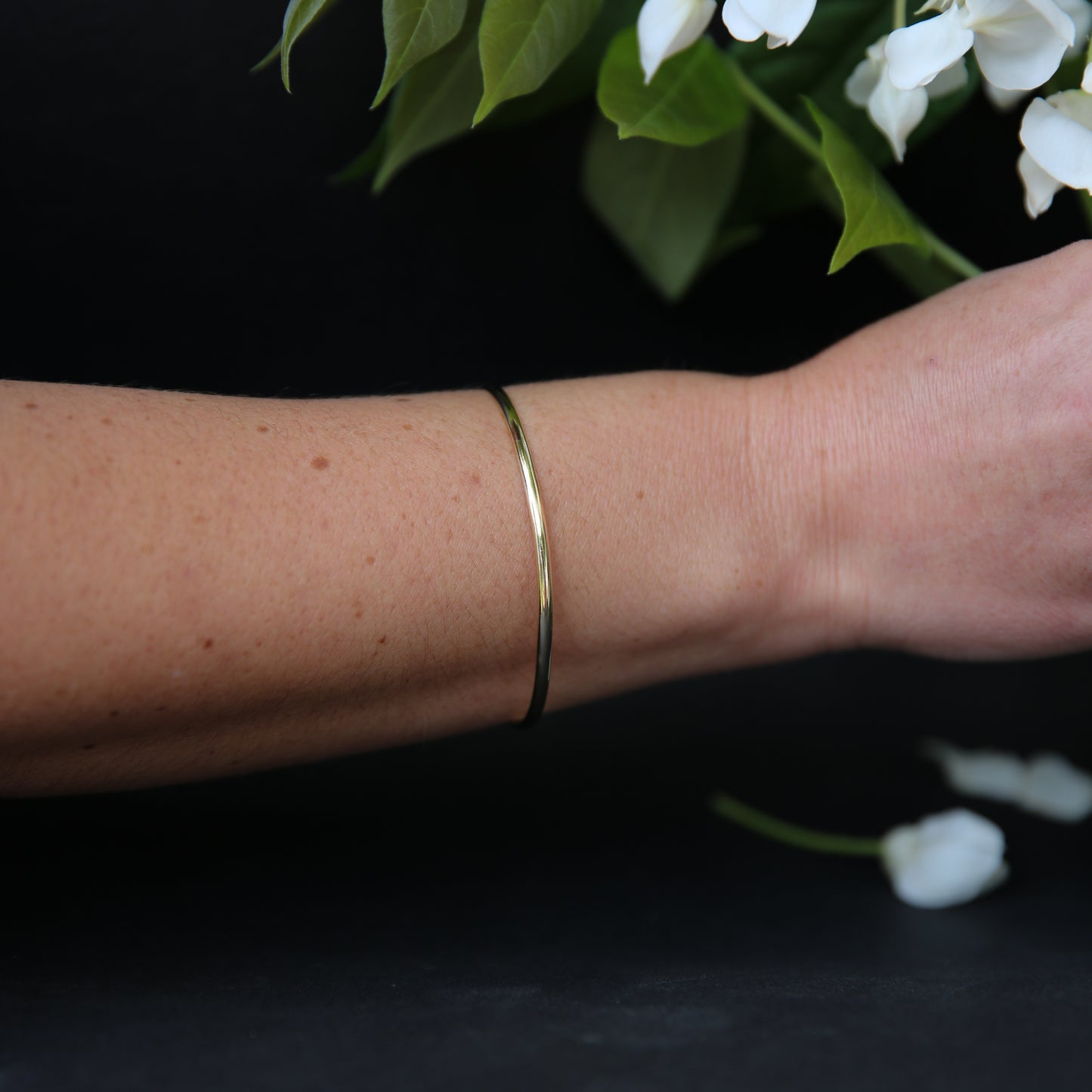 Gold bracelet on a wrist with white flowers in the background