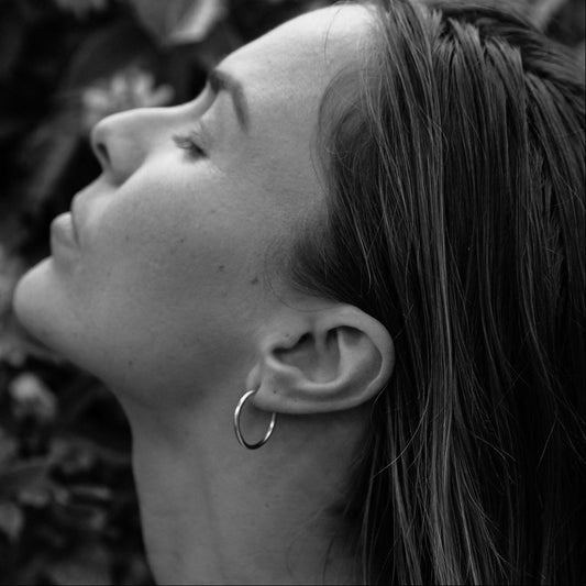 A close-up image of a woman's face with her eyes closed, wearing the Curved Hoops earrings mentioned in the product description.