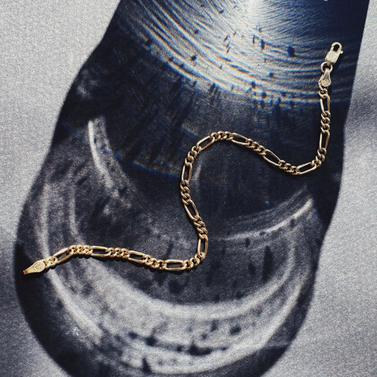 A gold Figaro chain bracelet displayed on a flat surface.
