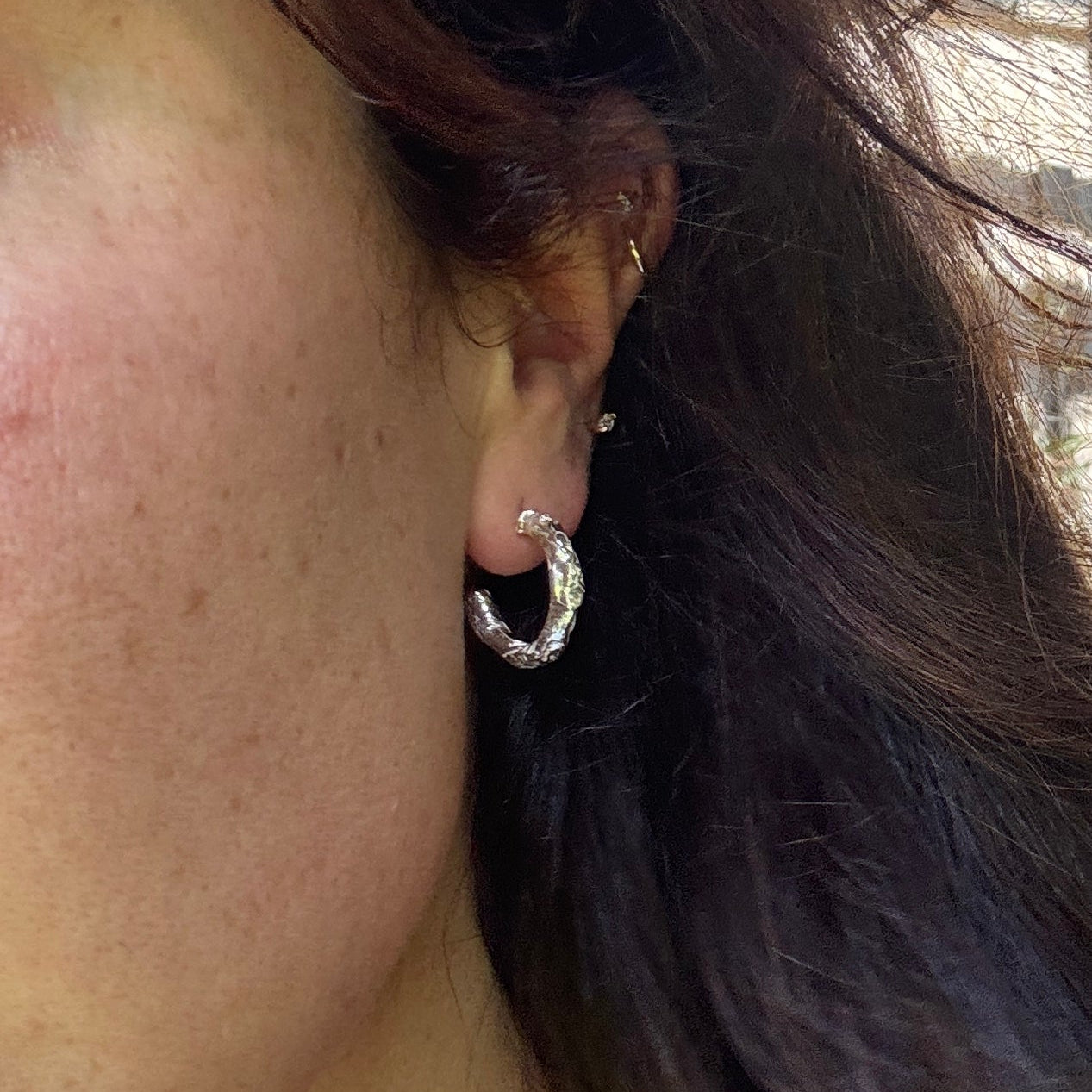 Close-up of an ear wearing a silver hoop earring with hair partially covering the face.