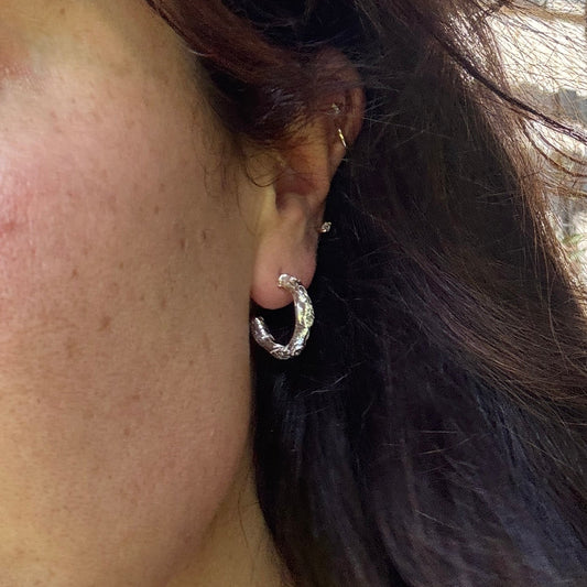 Close-up of an ear wearing a silver hoop earring with hair partially covering the face.