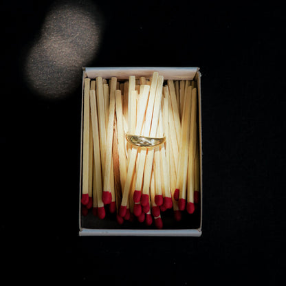 Slim signet ring in a matchbox with matches on a black background