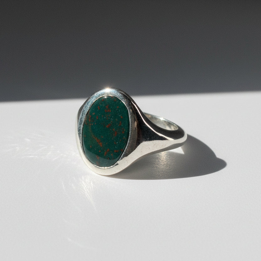 Silver ring with a green stone on a white surface with a dark background