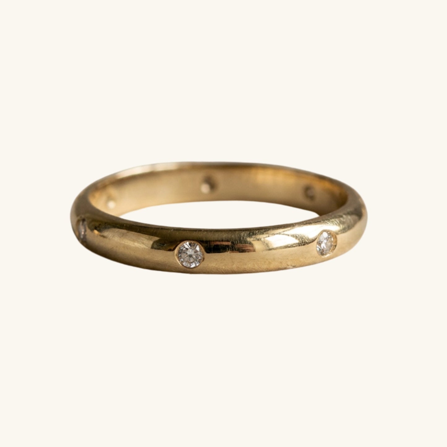 A yellow gold band ring featuring three small, round-cut clear gemstones spaced along the front, set against a plain off-white background.