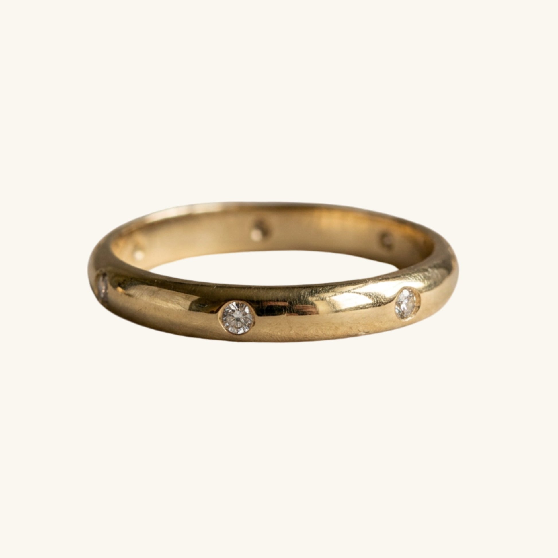 A yellow gold band ring featuring three small, round-cut clear gemstones spaced along the front, set against a plain off-white background.
