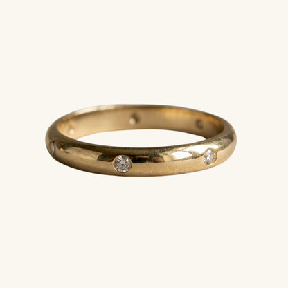 A yellow gold band ring featuring three small, round-cut clear gemstones spaced along the front, set against a plain off-white background.