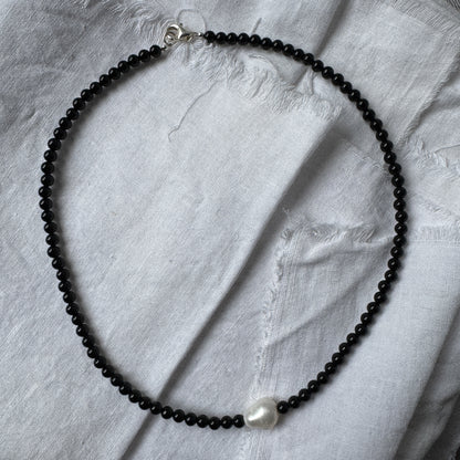 Necklace with black beads and a pearl on a light gray fabric background