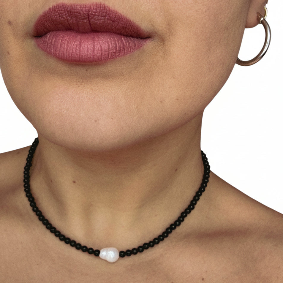 Close-up of a person wearing a black beaded necklace with a white pendant.