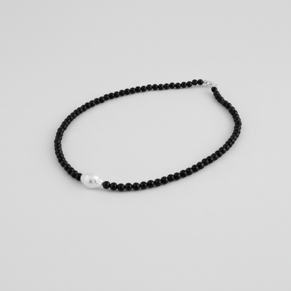 Black beaded necklace with a pearl pendant on a light gray background