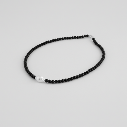 Black beaded necklace with a pearl pendant on a light gray background
