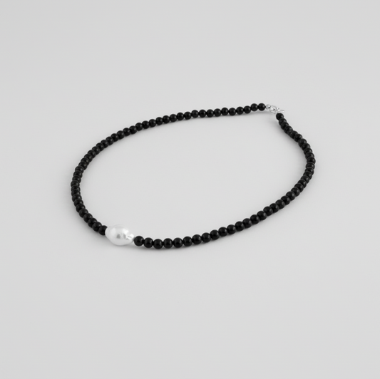 Black beaded necklace with a pearl pendant on a light gray background