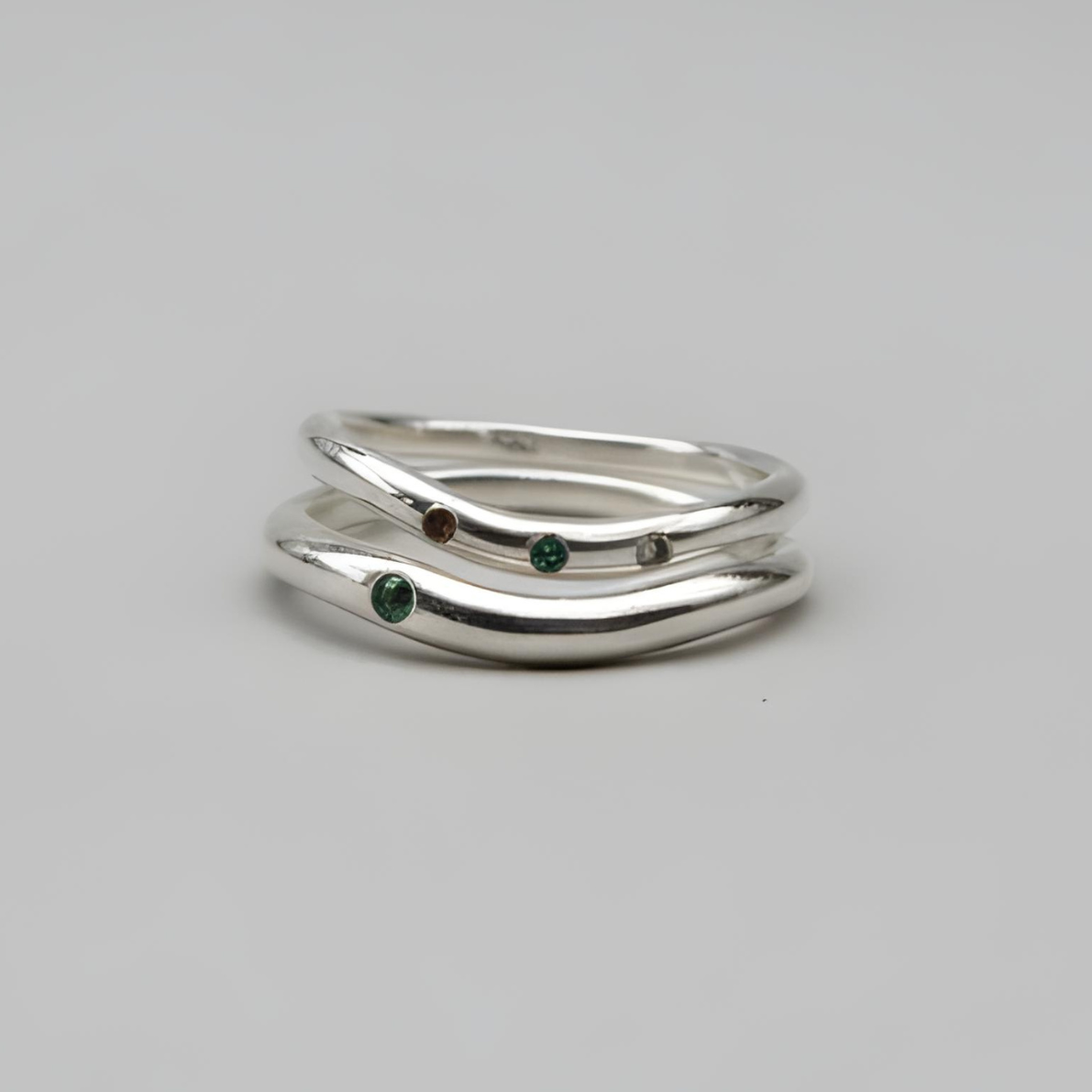Silver ring with green gemstones on a gray background