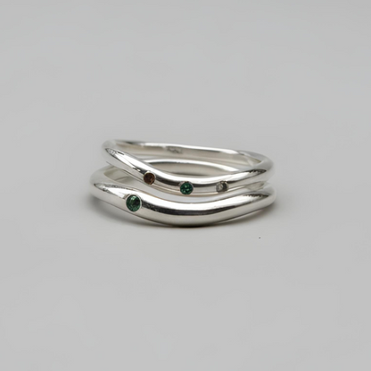 Silver ring with green gemstones on a gray background