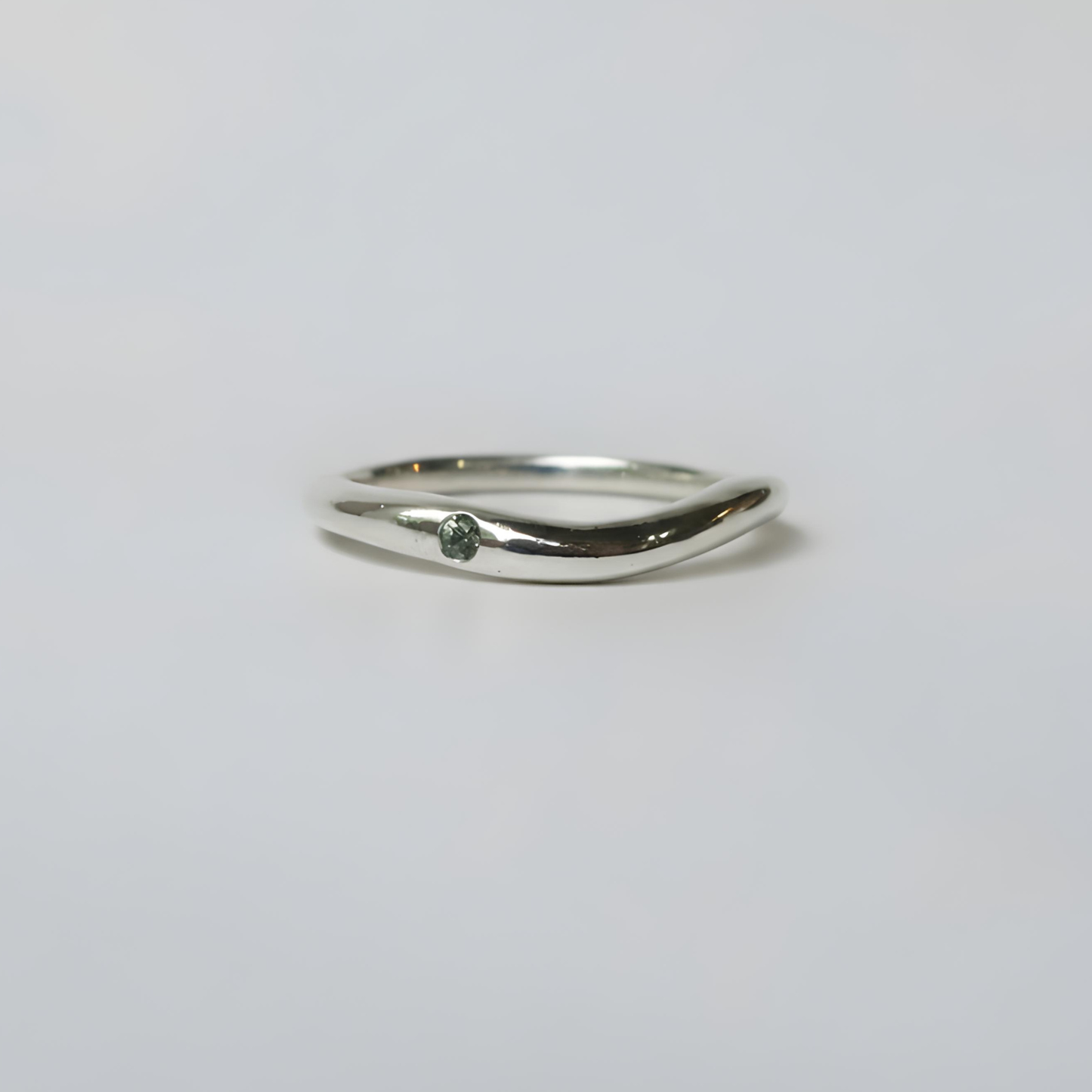 Silver ring with a small diamond on a light gray background