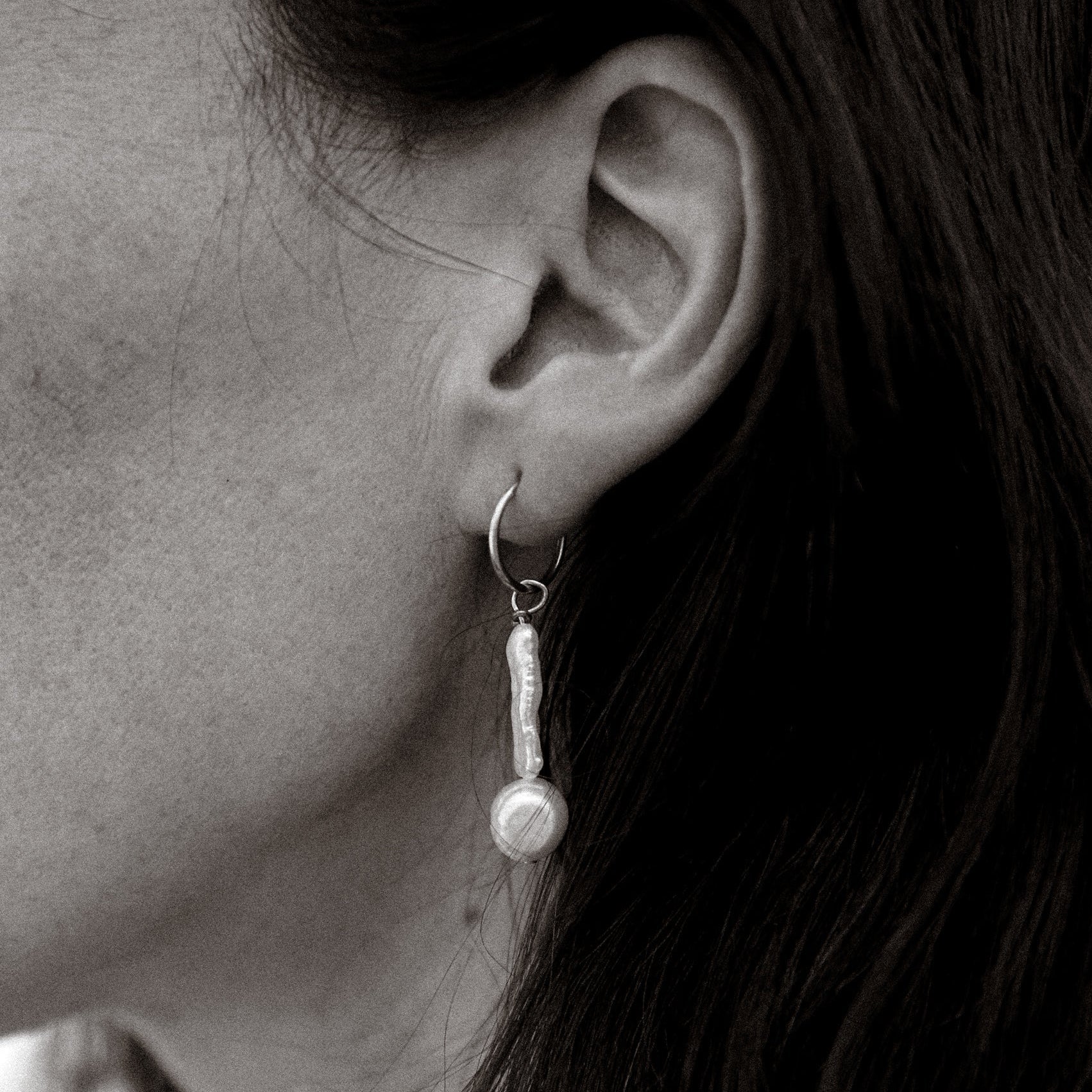 Close-up of an ear wearing a pearl earring with dark hair.