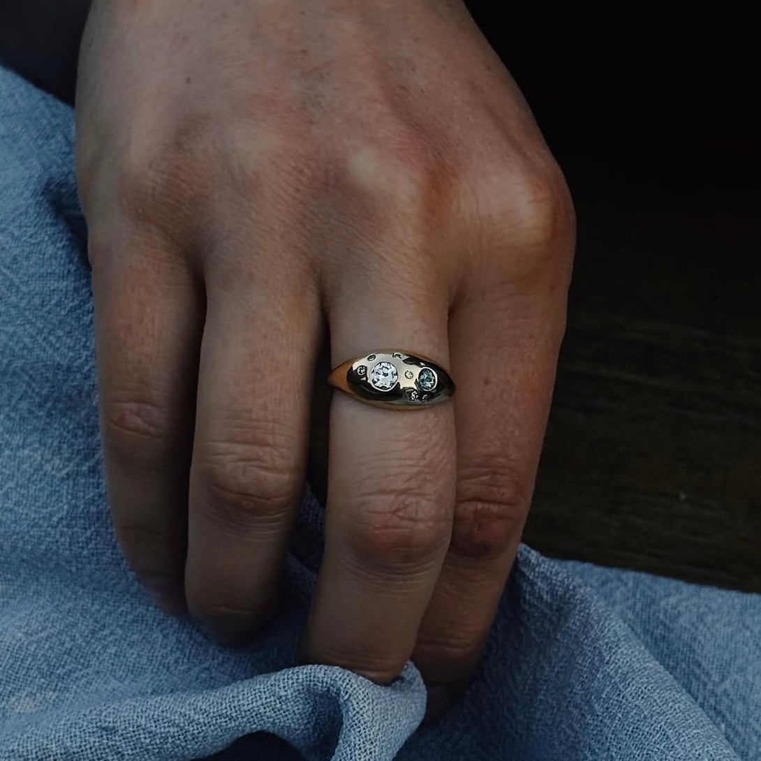 Hand wearing a gold ring with a diamond on a blue fabric background