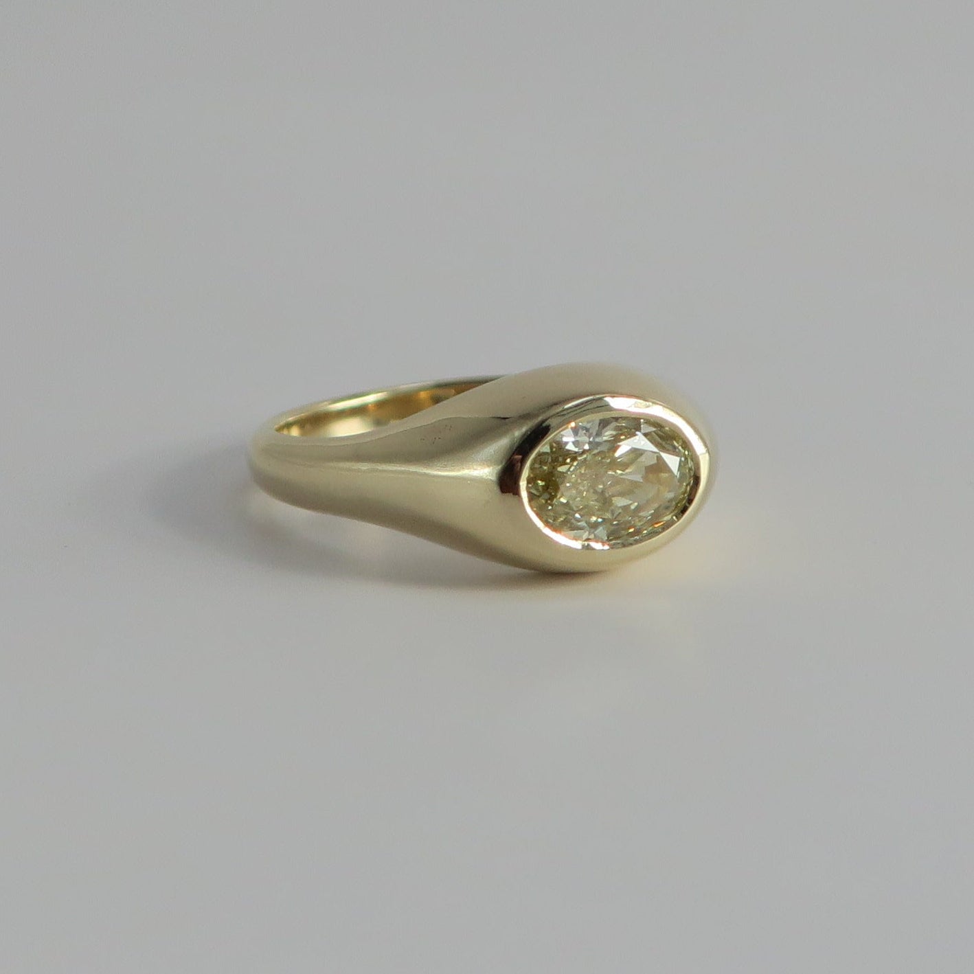 A small gold signet ring with a round bezel-set clear gemstone, photographed on a plain light gray background.