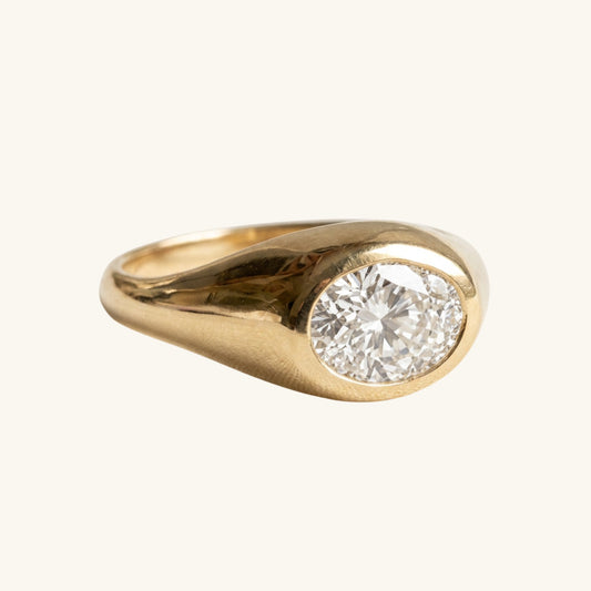A yellow gold ring featuring a large, oval brilliant-cut diamond set in a polished bezel-like oval shape, shown against a solid off-white background.