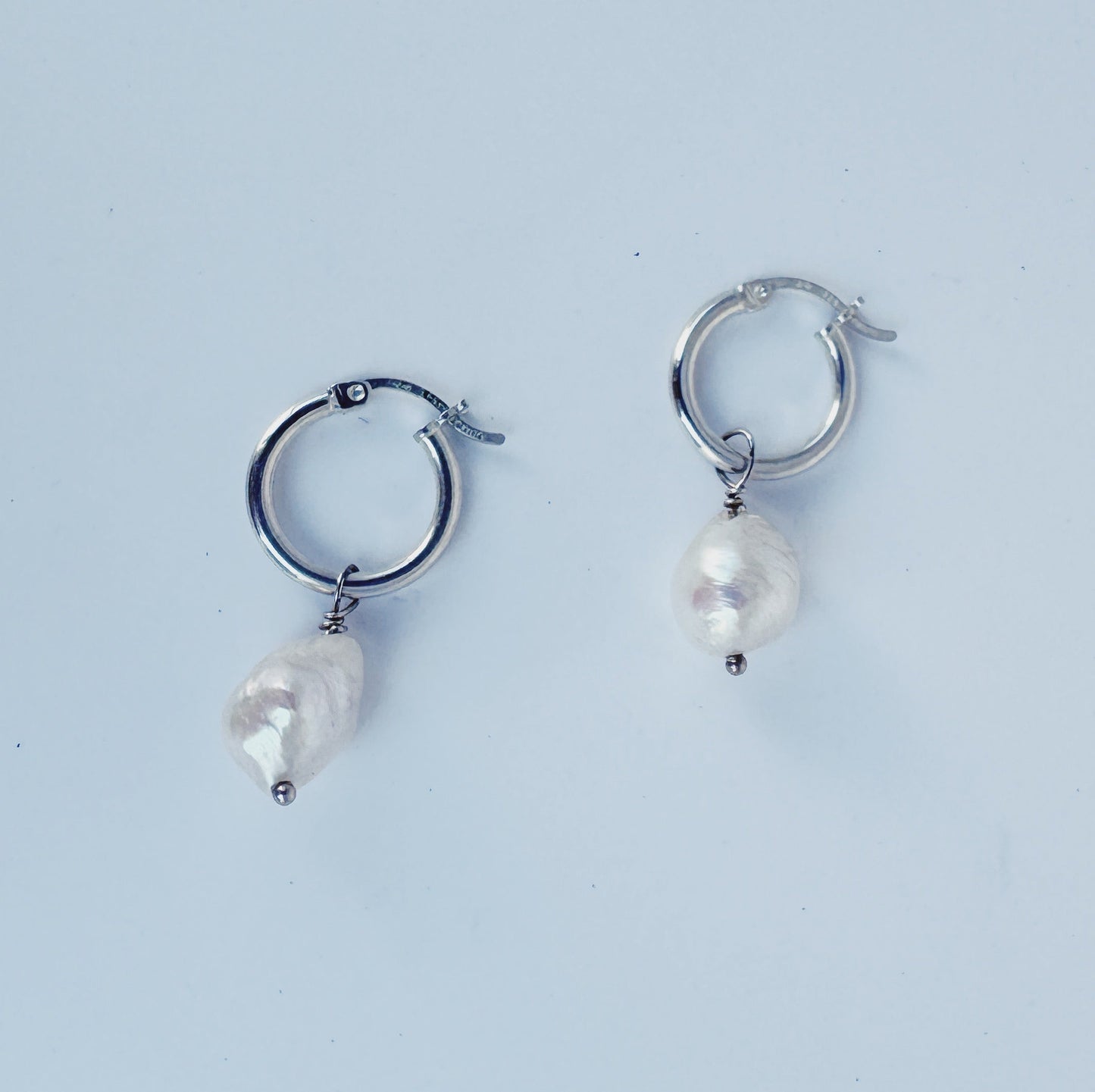 Pair of silver hoop earrings with pearl-like beads on a light blue background
