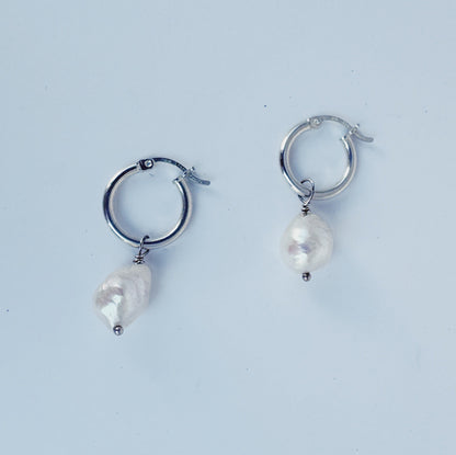Pair of silver hoop earrings with pearl-like beads on a light blue background