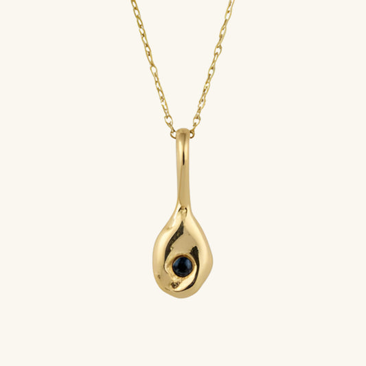 Gold pendant necklace with a blue gemstone on a cream background