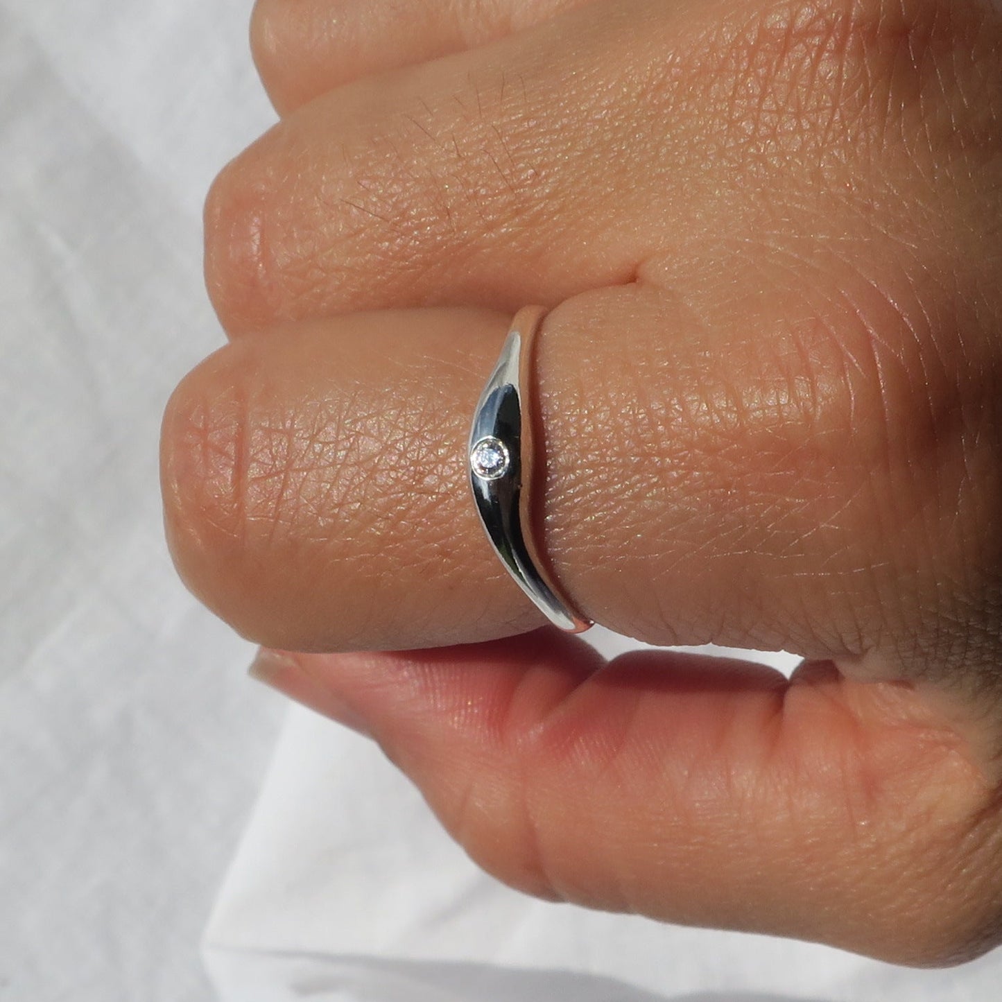 Silver ring with a diamond on a person's finger against a white background