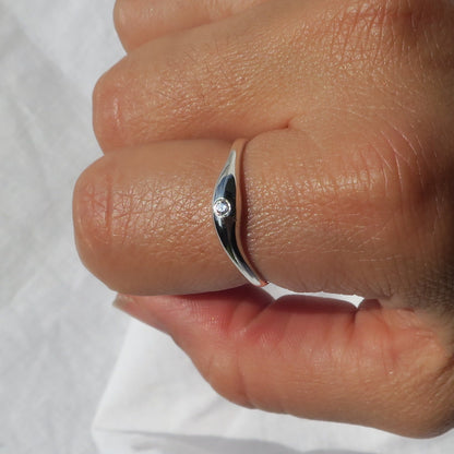 Silver ring with a diamond on a person's finger against a white background