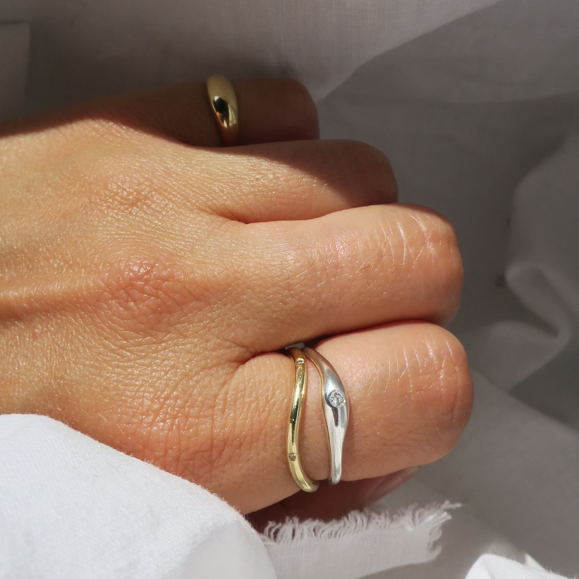 Hand wearing gold & silver rings on a light fabric background