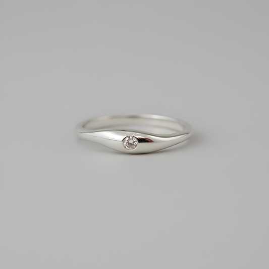 Silver ring with a small diamond on a gray background