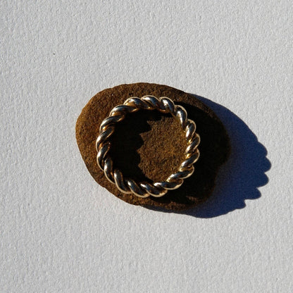 Gold ring with rope design on a brown stone against a light gray background