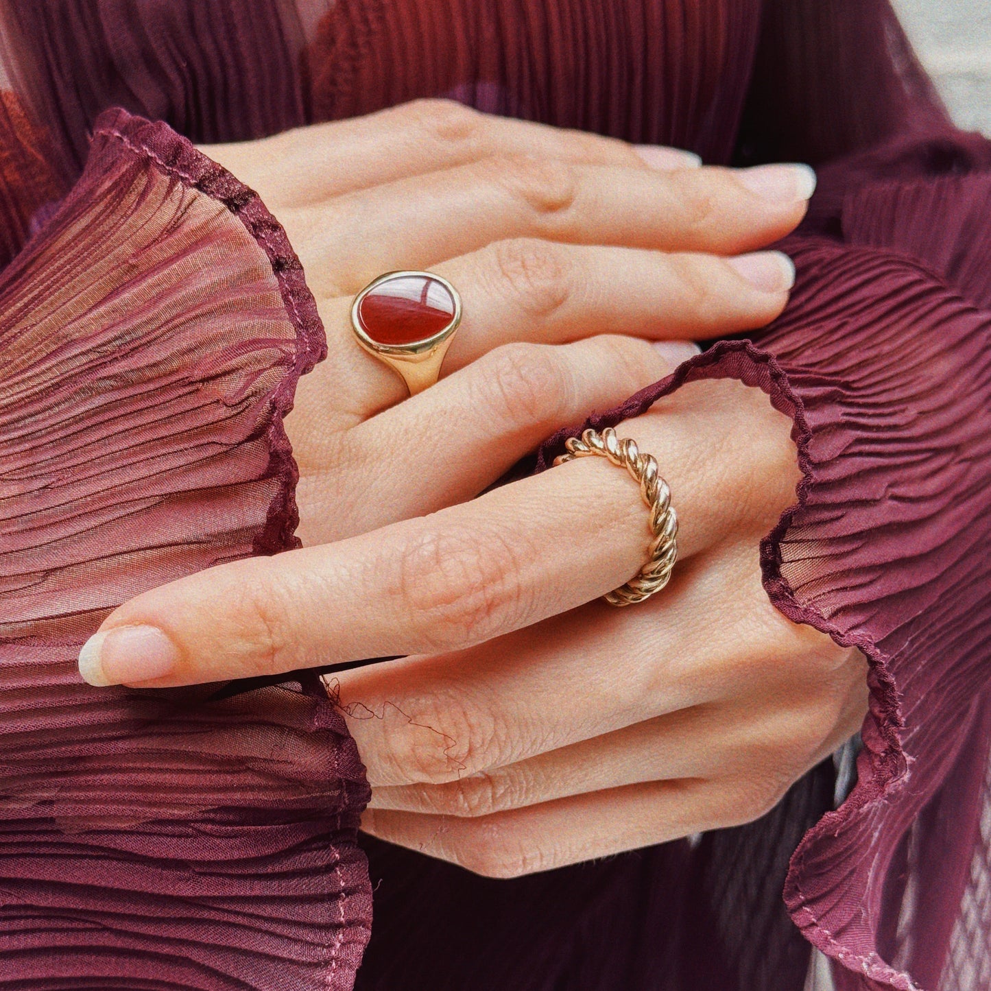 Hands intertwined with a rope band and carnelian red and gold signet ring. 
