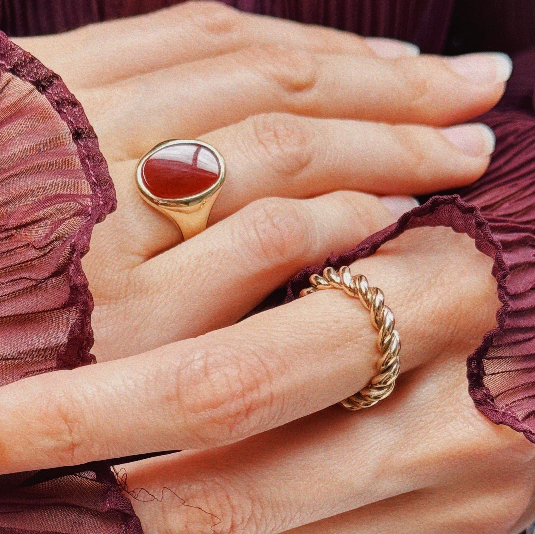 Hands intertwined with a rope band and carnelian red and gold signet ring. 