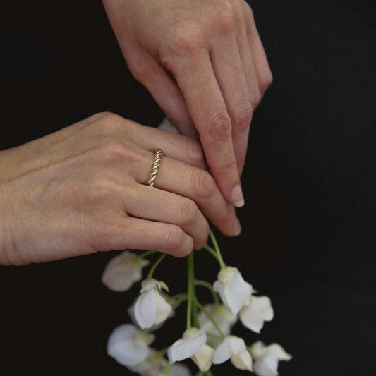 Close-up of hands with a gold ring holding white flowers against a black background