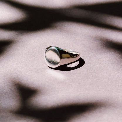 A classic round signet ring made of silver, displayed against a textured background.