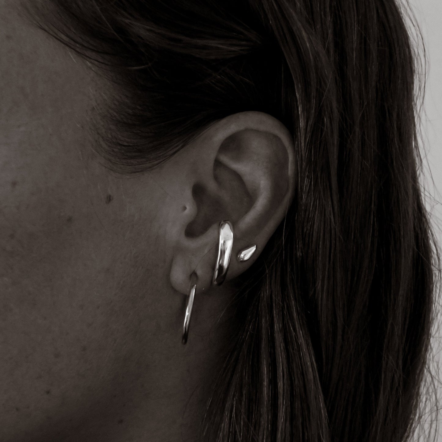 Close-up of an ear wearing two silver hoop earrings with a neutral background