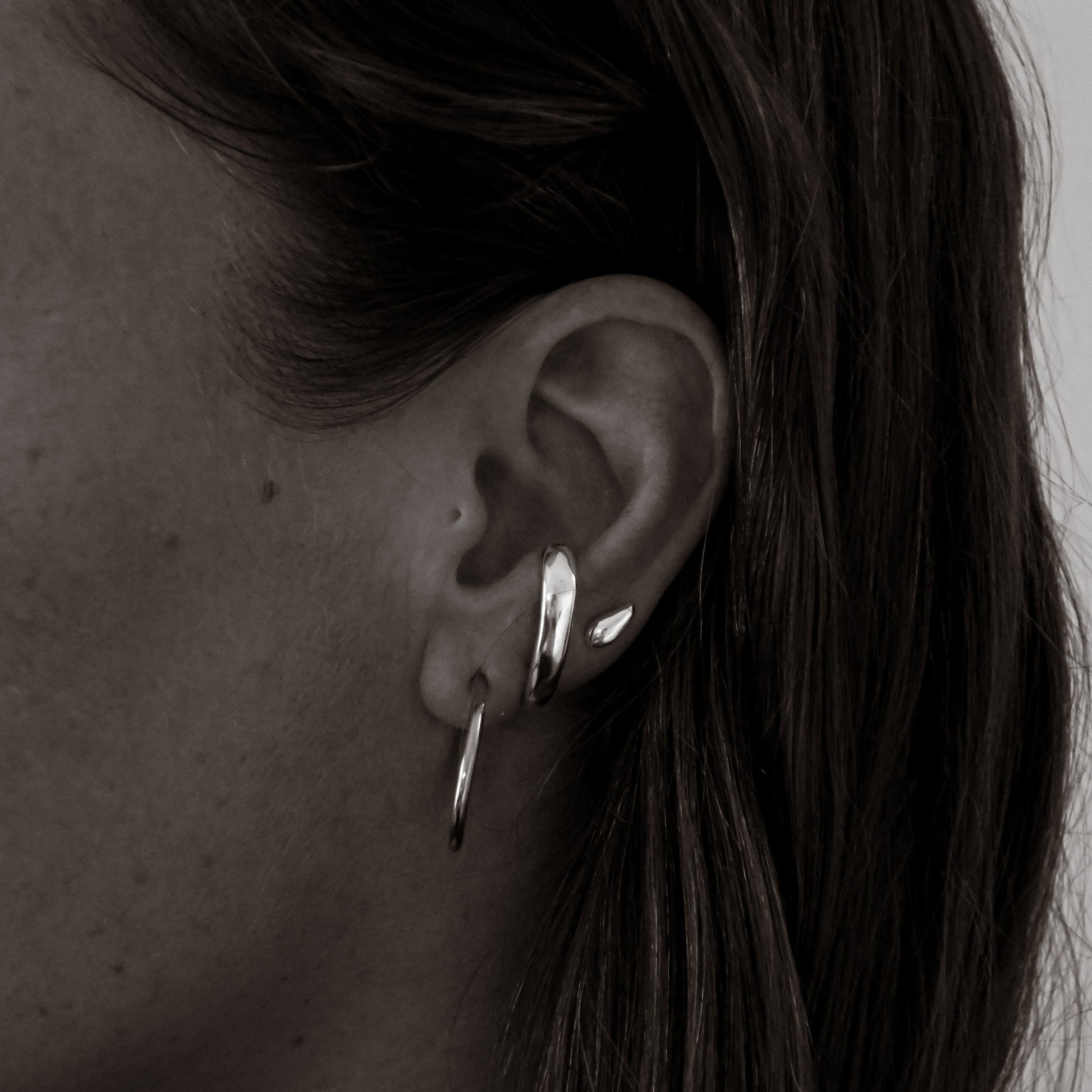 Close-up of an ear wearing two silver hoop earrings with a neutral background