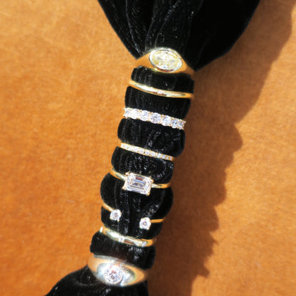 A close-up of a range of diamond rings in gold and silver with diamonds. Rings are thread through black velvet and sitting upon a burnt orange background. 