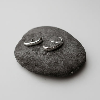 Two silver earrings on a gray stone surface